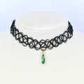 A black choker necklace with a pendant. The necklace is made of a series of interconnected black loops. A gold-colored pendant hangs from the center, featuring a teardrop-shaped green gemstone.