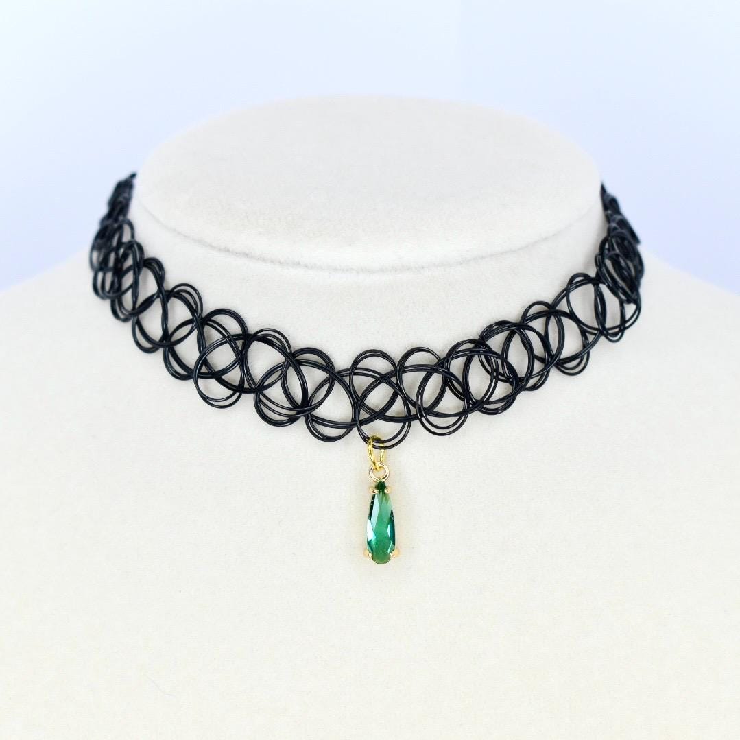 A black choker necklace with a pendant. The necklace is made of a series of interconnected black loops. A gold-colored pendant hangs from the center, featuring a teardrop-shaped green gemstone.