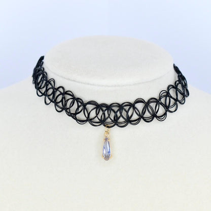 A black choker necklace with a pendant. The necklace is made of a black, stretchy material with a repeating circular design. A teardrop-shaped pendant hangs from the center, featuring a gold-colored setting and a light purple gemstone.