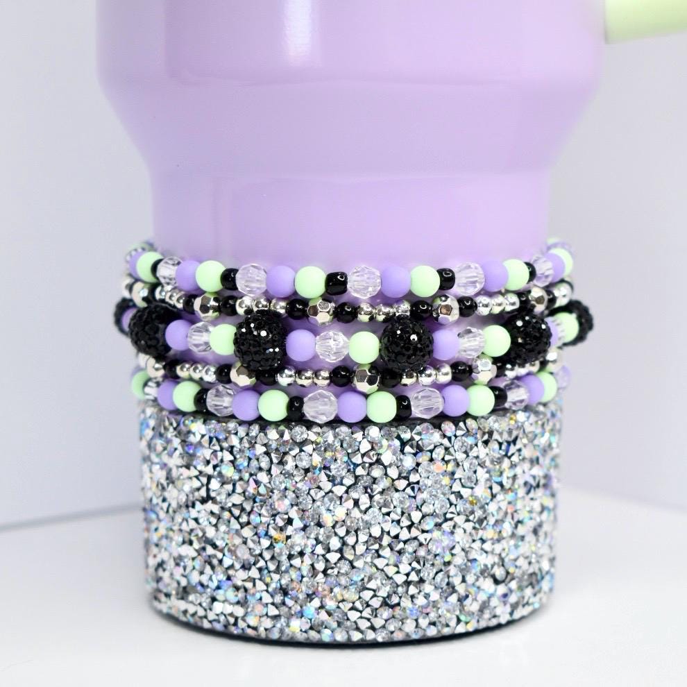 Beaded tumbler bracelet in pastel purple, mint green, black, and silver shown on a lavender tumbler with rhinestone base. Features faceted clear beads, shiny silver spacers, and textured black beads for a bold, colorful look.