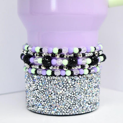 Beaded tumbler bracelet in pastel purple, mint green, black, and silver shown on a lavender tumbler with rhinestone base. Features faceted clear beads, shiny silver spacers, and textured black beads for a bold, colorful look.