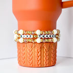 Three beaded bracelets with textured pearl, gold, and light brown beads around the pumpkin spice Stanley. The middle bracelet has letter beads that spell out GIVE THANKS. This bracelet trio is perfect for Fall.