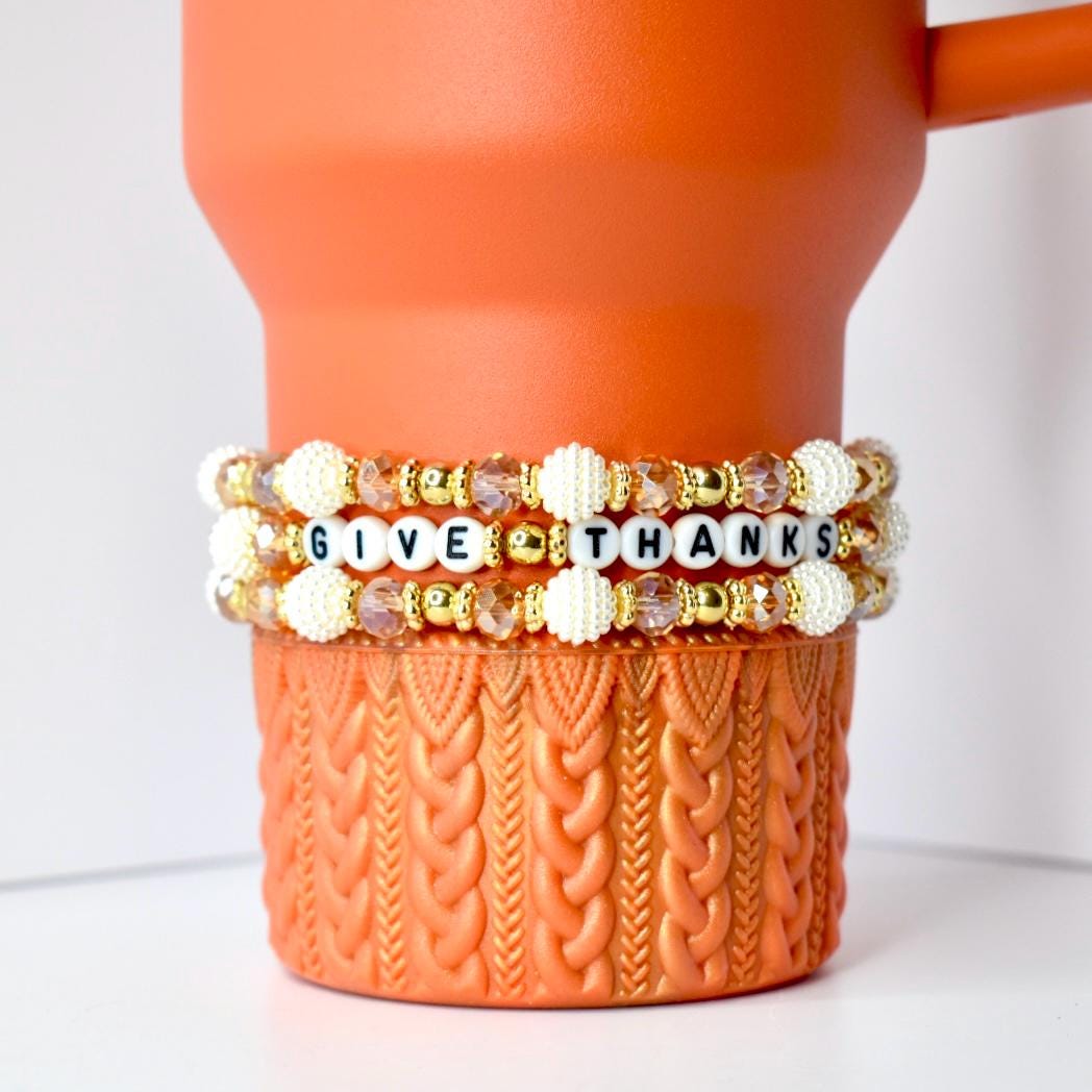 Three beaded bracelets with textured pearl, gold, and light brown beads around the pumpkin spice Stanley. The middle bracelet has letter beads that spell out GIVE THANKS. This bracelet trio is perfect for Fall.