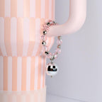 A pink beaded bracelet with silver accents and a mirrored disco ball charm. The bracelet is hanging on a light pink curved object, with a pink and white striped background.