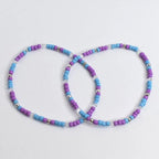 Two beaded bracelets. Each bracelet features a repeating pattern of purple, light blue, and clear beads, interspersed with silver-colored beads. The bracelets are circular and appear to be handmade, suitable for casual wear.
