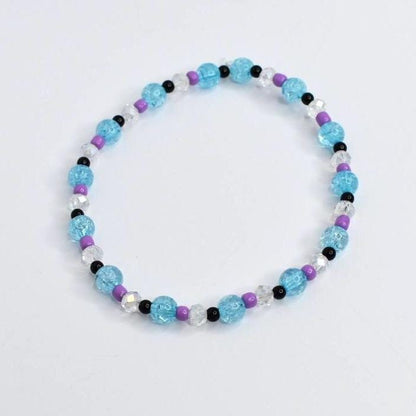 A beaded bracelet featuring light blue, purple, black, and clear beads. The bracelet has a mix of round and faceted beads, creating a colorful and textured accessory. The bracelet is on a white background.