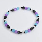 A beaded bracelet featuring a variety of colorful beads. The bracelet includes light blue, purple, black, and clear beads. The beads are strung together to form a circular shape. The bracelet is on a white background.