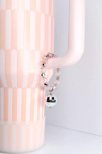 A pink and white Stanley tumbler with a handle bracelet. The bracelet features pink beads, silver accents, and a mirrored disco ball charm. The overall aesthetic is playful and decorative.