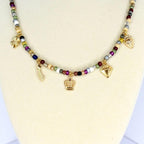 A beaded necklace with a variety of colorful beads and gold-colored charms. The charms include a crown, a diamond, a shooting star, a strawberry, and a four-leaf clover. The necklace is displayed on a white surface.