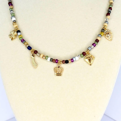 A beaded necklace with a variety of colorful beads and gold-colored charms. The charms include a crown, a diamond, a shooting star, a strawberry, and a four-leaf clover. The necklace is displayed on a white surface.
