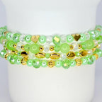 Four beaded bracelets in shades of green and gold. The bracelets feature a variety of beads, including round, faceted, and heart-shaped beads. The bracelets are stacked on top of each other.