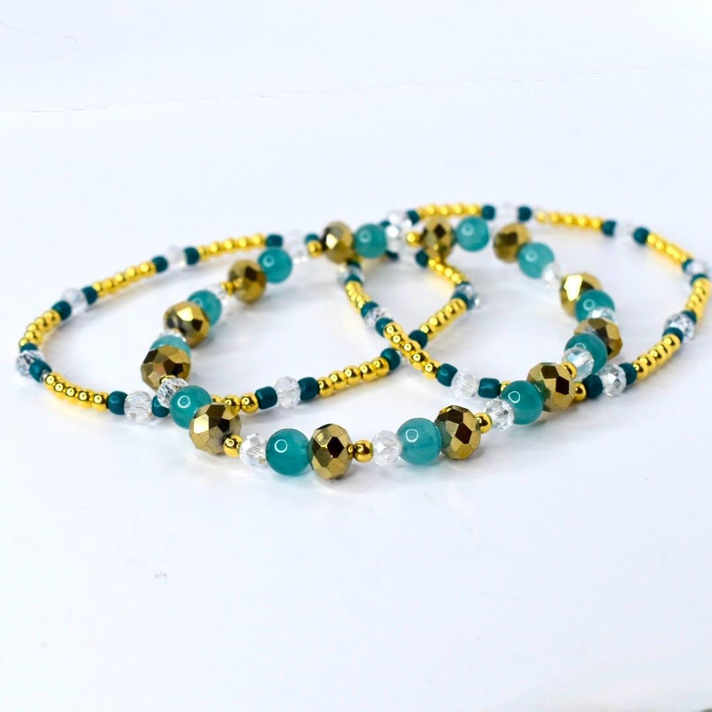 Gold, teal, and clear beaded tumbler bracelet laid flat to show full length. Features faceted metallic gold beads, smooth teal beads, and sparkling clear accents with gold spacer beads.
