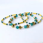 Gold, teal, and clear beaded tumbler bracelet laid flat to show full length. Features faceted metallic gold beads, smooth teal beads, and sparkling clear accents with gold spacer beads.
