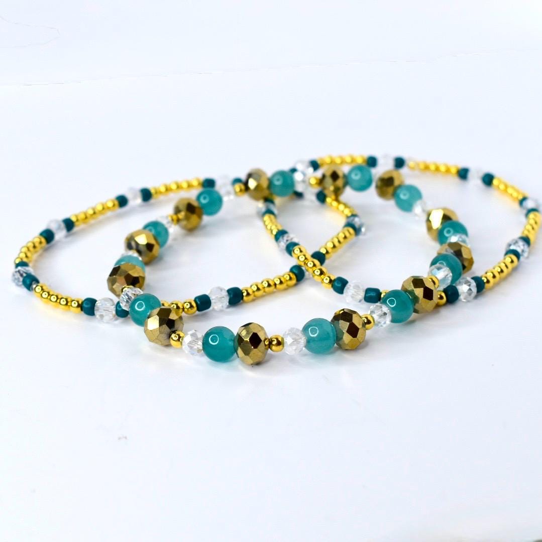 Gold, teal, and clear beaded tumbler bracelet laid flat to show full length. Features faceted metallic gold beads, smooth teal beads, and sparkling clear accents with gold spacer beads.