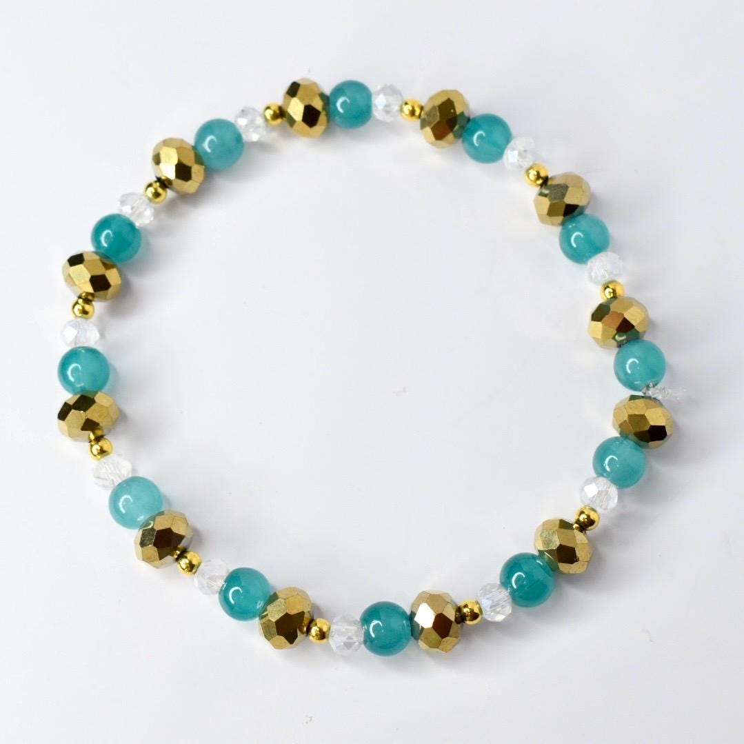 Gold, teal, and clear beaded tumbler bracelet displayed in a circular shape. Features metallic gold faceted beads, smooth teal beads, and sparkling clear crystals for a bold, elegant look.