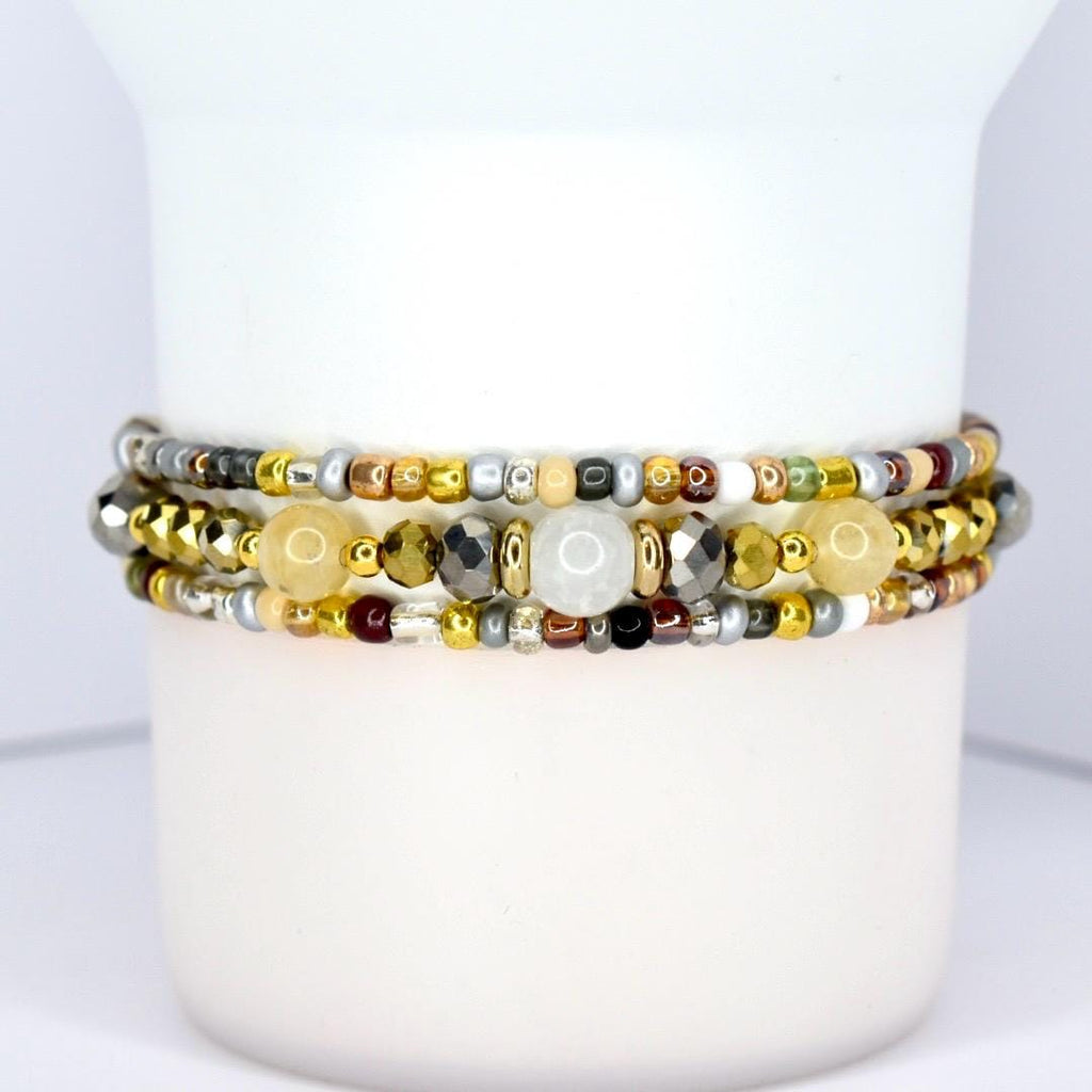 Three beaded bracelets with a variety of beads in gold, silver, and neutral tones. The bracelets are stacked together, showcasing a mix of textures and colors, including metallic and gemstone beads.