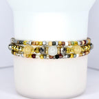 Three beaded bracelets with a variety of beads in gold, silver, and neutral tones. The bracelets are stacked together, showcasing a mix of textures and colors, including metallic and gemstone beads.