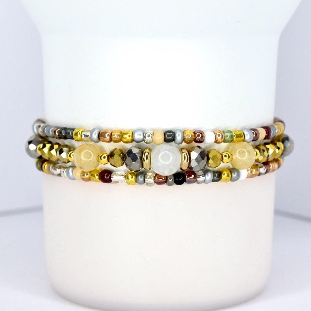 Three beaded bracelets with a variety of beads in gold, silver, and neutral tones. The bracelets are stacked together, showcasing a mix of textures and colors, including metallic and gemstone beads.