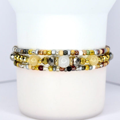 Three beaded bracelets with a variety of beads in gold, silver, and neutral tones. The bracelets are stacked together, showcasing a mix of textures and colors, including metallic and gemstone beads.