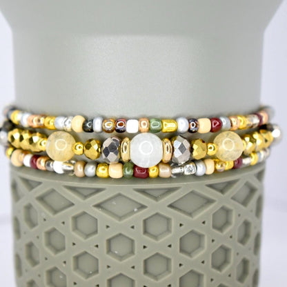 Three beaded bracelets with a variety of colors and textures. The bracelets feature gold, silver, and bronze beads, along with larger, round, and faceted beads. The bracelets are stacked on top of a gray, textured surface.