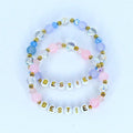 Two beaded bracelets with the word 'BESTIE' spelled out in gold letters. The bracelets feature a combination of white, pink, light blue, and clear beads. The beads are arranged in a pattern with gold accents, creating a friendship-themed accessory.