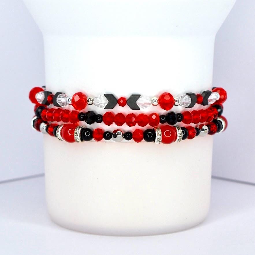Three beaded bracelets stacked together. The top bracelet features red and black beads with silver accents and black arrow-shaped beads. The middle bracelet has red faceted beads and black beads. The bottom bracelet has red and black beads with silver accents and a red bead with a silver band.
