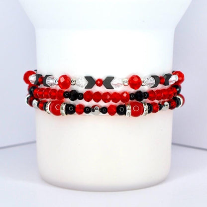 Three beaded bracelets stacked together. The top bracelet features red and black beads with silver accents and black arrow-shaped beads. The middle bracelet has red faceted beads and black beads. The bottom bracelet has red and black beads with silver accents and a red bead with a silver band.