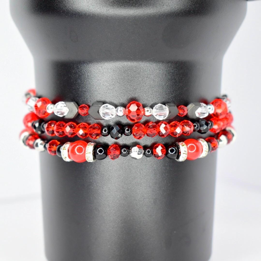 Three beaded bracelets in red, black, and silver. The top bracelet features red and clear beads with black accents. The middle bracelet has red and black beads. The bottom bracelet has red and black beads with silver accents and a large red bead.