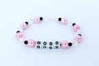 A pink and white beaded bracelet with the word 'BOSS' spelled out in white letter beads. The bracelet features pink pearl beads, clear crystal beads, and small black beads. The bracelet is displayed on a white surface.