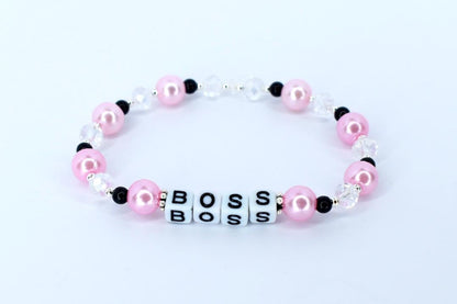 A pink and white beaded bracelet with the word 'BOSS' spelled out in white letter beads. The bracelet features pink pearl beads, clear crystal beads, and small black beads. The bracelet is displayed on a white surface.