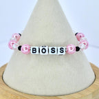 A pink and white beaded bracelet spelling out the word "BOSS". The bracelet features pink pearl beads, clear crystal beads, and black accent beads. The letters are white with black lettering.