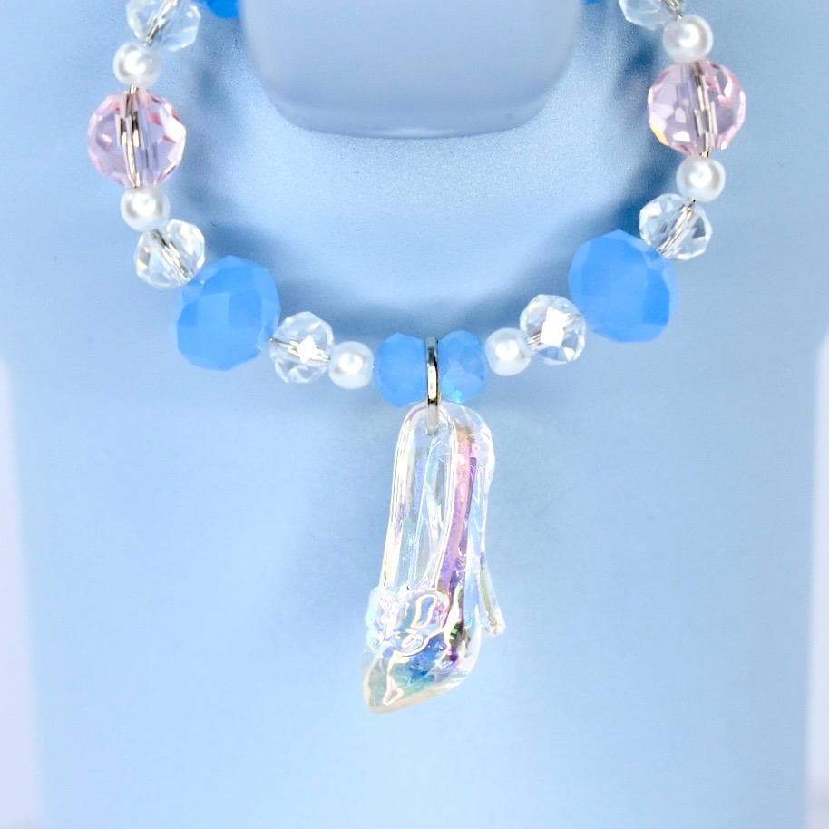 A blue beaded tumbler handle charm with a clear, iridescent high-heeled shoe pendant. The handle charm features light blue, pink, and clear beads, with small white pearls. The pendant is a detailed miniature of a glass slipper.