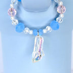 A blue beaded tumbler handle charm with a clear, iridescent high-heeled shoe pendant. The handle charm features light blue, pink, and clear beads, with small white pearls. The pendant is a detailed miniature of a glass slipper.