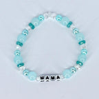 A beaded bracelet featuring light blue and clear beads. The bracelet includes the word "MAMA" spelled out in white letter beads. The beads are strung together with a clear elastic cord.