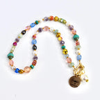 A colorful beaded necklace with a variety of shapes and sizes of beads in shades of pink, blue, green, yellow, and gold. A gold-colored charm with the words "YOU ARE MY sunshine" hangs from the necklace, along with a white pearl.
