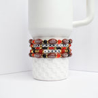Four beaded bracelets stacked on a white ceramic mug. The bracelets feature a combination of red, black, and gold beads. Some beads are shaped like footballs, and others spell out 'SAN FRANCISCO 49ERS'.