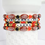 Stack of beaded bracelets featuring football-shaped beads and letter beads spelling 'SAN FRANCISCO' and '49ERS'. The bracelets have a color scheme of brown, red, black, gold, and white. The football beads have white stitching.