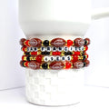 A stack of beaded bracelets featuring a football theme. The bracelets are primarily brown, red, black, and gold. Each bracelet has football-shaped beads, letter beads spelling 'SAN FRANCISCO 49ERS', and various round beads. The bracelets are stacked on a white, textured surface.