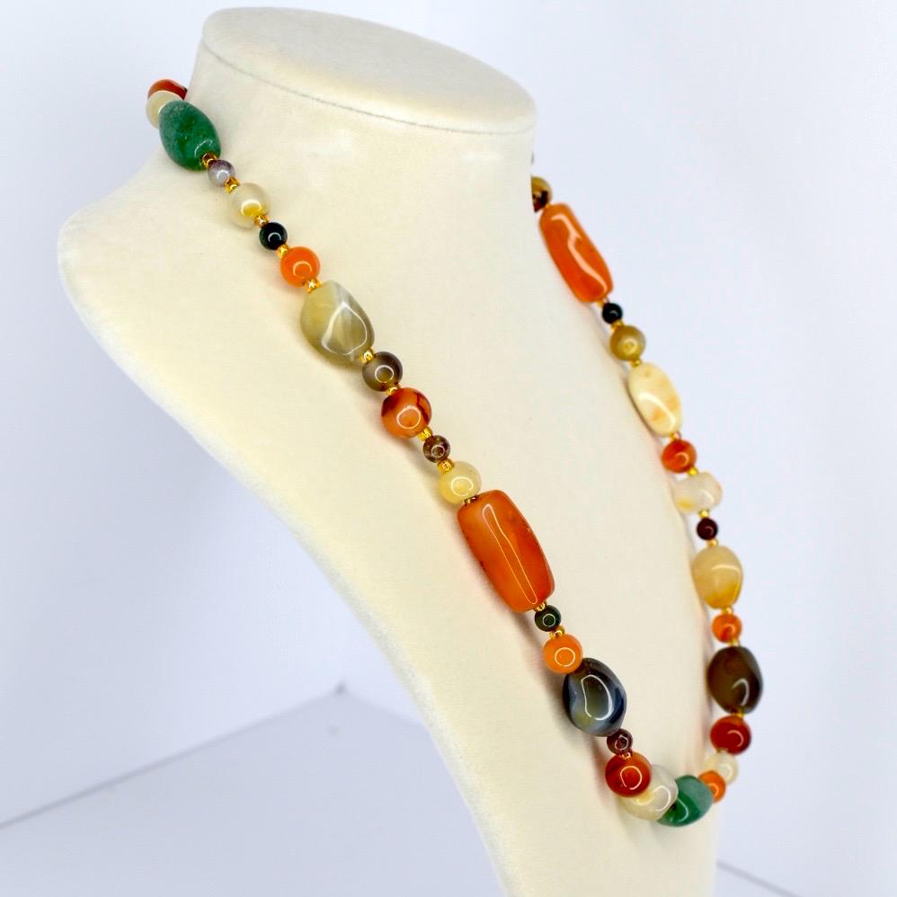Chunky gemstone necklace with bold orange, green, and brown beads arranged on a cream jewelry display.