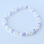 A delicate bracelet featuring a mix of iridescent and white beads, interspersed with small, faceted purple beads. The bracelet is strung together, creating a flexible and elegant accessory.