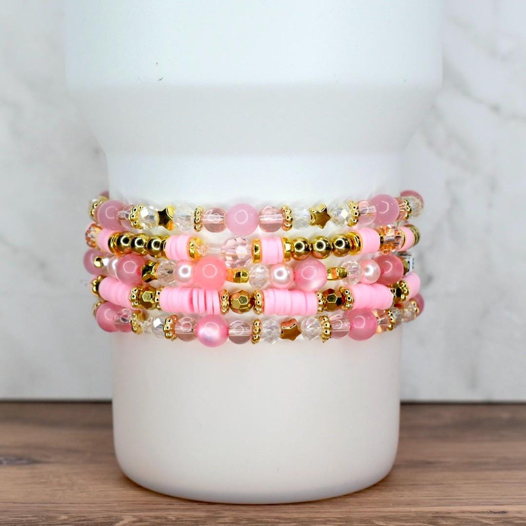 Handmade pink bracelet stack with gold accents, pearls, and clear beads, shown wrapped around a tumbler cup.