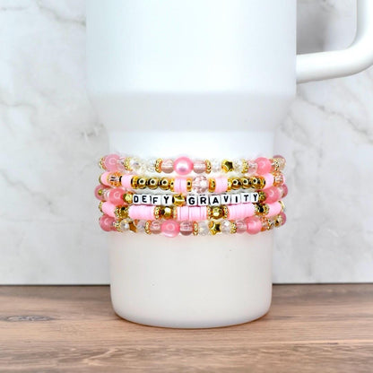 Handmade pink and gold beaded tumbler bracelets with pearls, clear beads, and star accents, wrapped around a cup.
