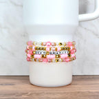 Handmade pink and gold beaded tumbler bracelets with pearls, clear beads, and star accents, wrapped around a cup.