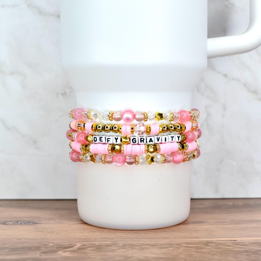 Handmade pink and gold beaded tumbler bracelets with pearls, clear beads, and star accents, wrapped around a cup.