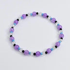 A beaded bracelet featuring a mix of purple, clear, black, and light blue beads. The bracelet is made with crackle-style purple beads, interspersed with clear, black, and light blue beads. This stretch bracelet is a piece of jewelry.