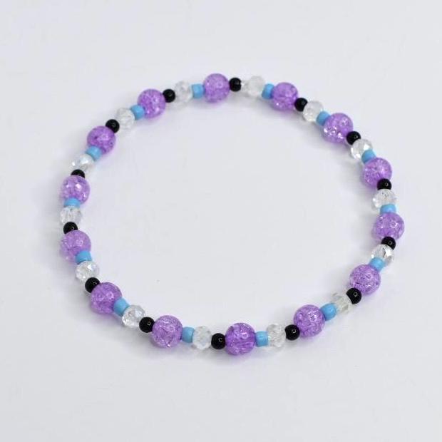 A beaded bracelet featuring a mix of purple, clear, black, and light blue beads. The bracelet is made with crackle-style purple beads, interspersed with clear, black, and light blue beads. This stretch bracelet is a piece of jewelry.