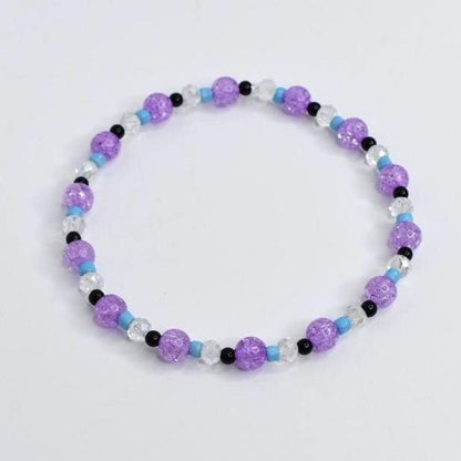 A beaded bracelet featuring a mix of purple, clear, black, and light blue beads. The bracelet is made with crackle-style purple beads, interspersed with clear, black, and light blue beads. This stretch bracelet is a piece of jewelry.