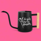 Black watering can with a long, curved spout and a wooden handle. The can features white text that reads 'it's your time to blossom' with a floral design. The handle is made of light-colored wood, and the can has a sleek, modern design, suitable for indoor or outdoor gardening.