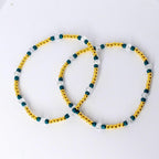 Simple gold, teal, and clear beaded tumbler bracelet shown flat. Features shiny gold spacer beads, teal accent beads, and faceted clear crystals in a lightweight minimalist design.