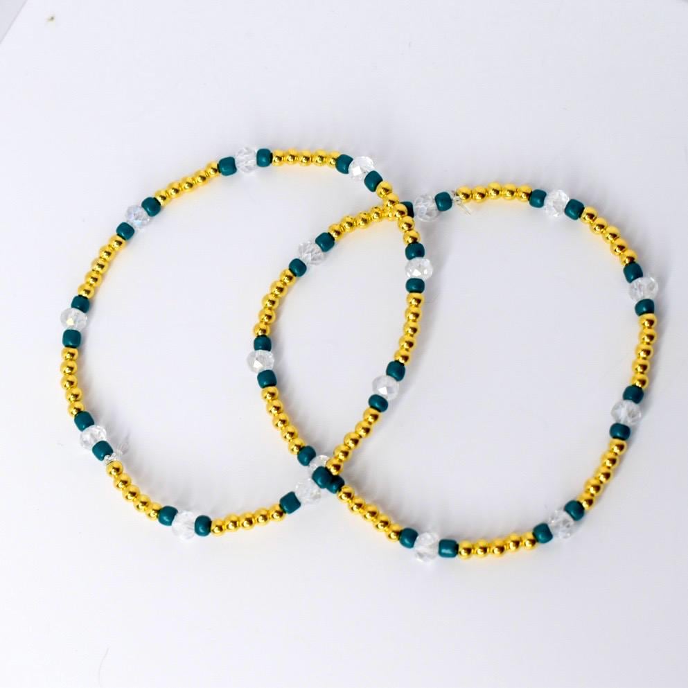 Simple gold, teal, and clear beaded tumbler bracelet shown flat. Features shiny gold spacer beads, teal accent beads, and faceted clear crystals in a lightweight minimalist design.